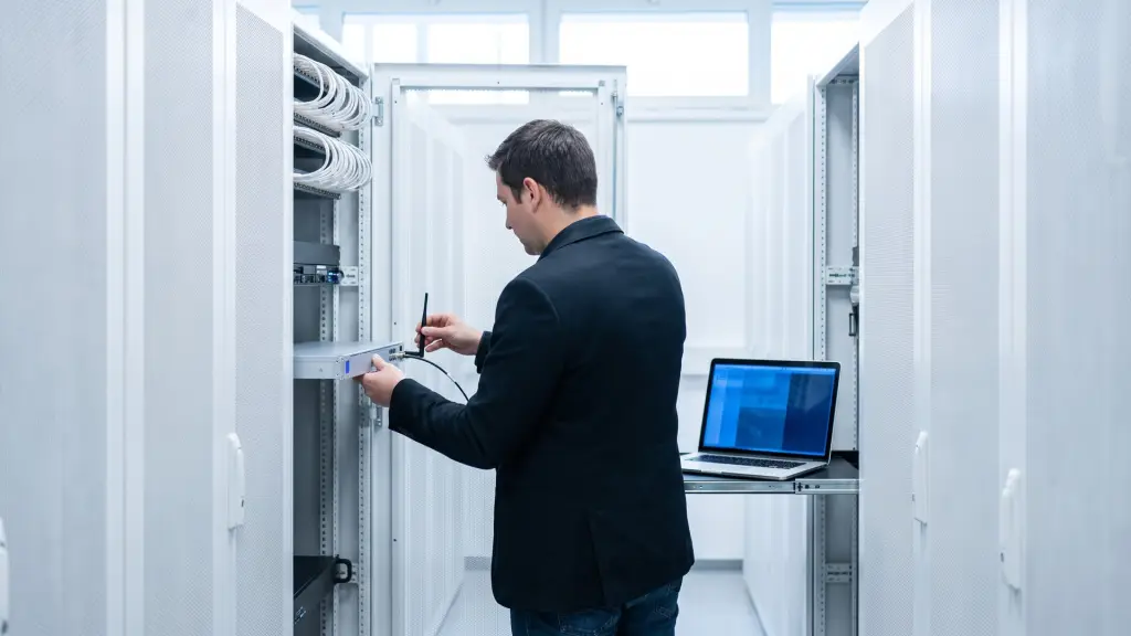 Un tecnico collega il cavo di un'antenna a un apparato di rete in un rack bianco, con un portatile su un ripiano estraibile
