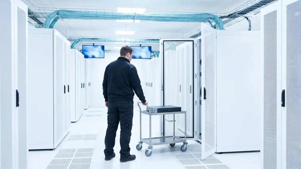 Un tecnico di spalle spinge un carrello con un server verso un rack aperto, in una sala dati bianca con fibre azzurre