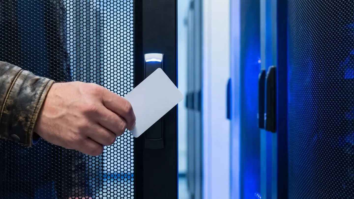 Una mano avvicina un badge bianco al lettore sulla porta di un armadio rack