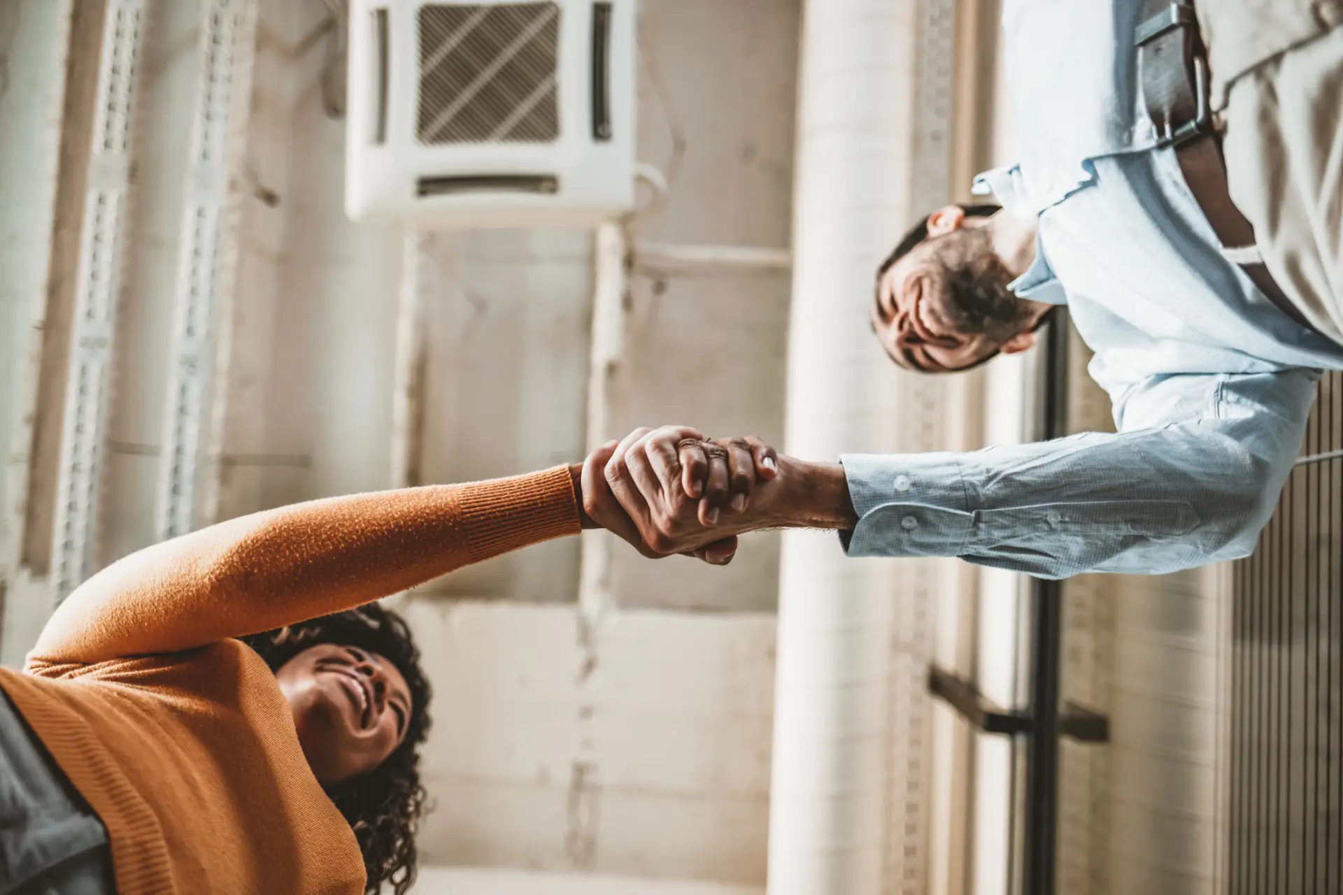 Due persone si stringono la mano in un ufficio, in controluce davanti a una vetrata.