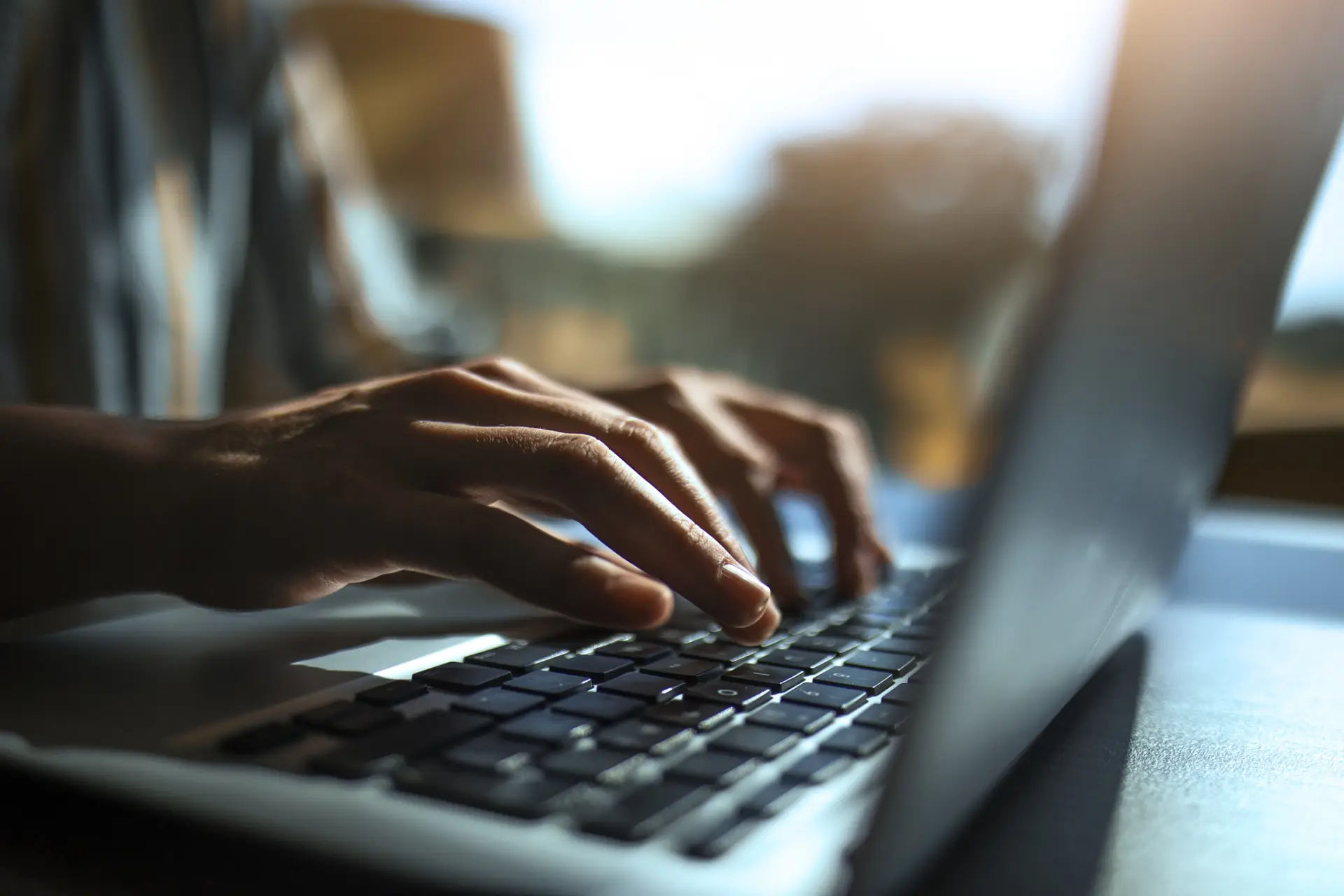 Mani su una tastiera di laptop, illuminate dalla luce di una finestra alle spalle.