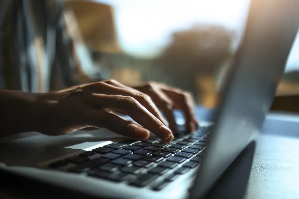 Mani su una tastiera di laptop, illuminate dalla luce di una finestra alle spalle.